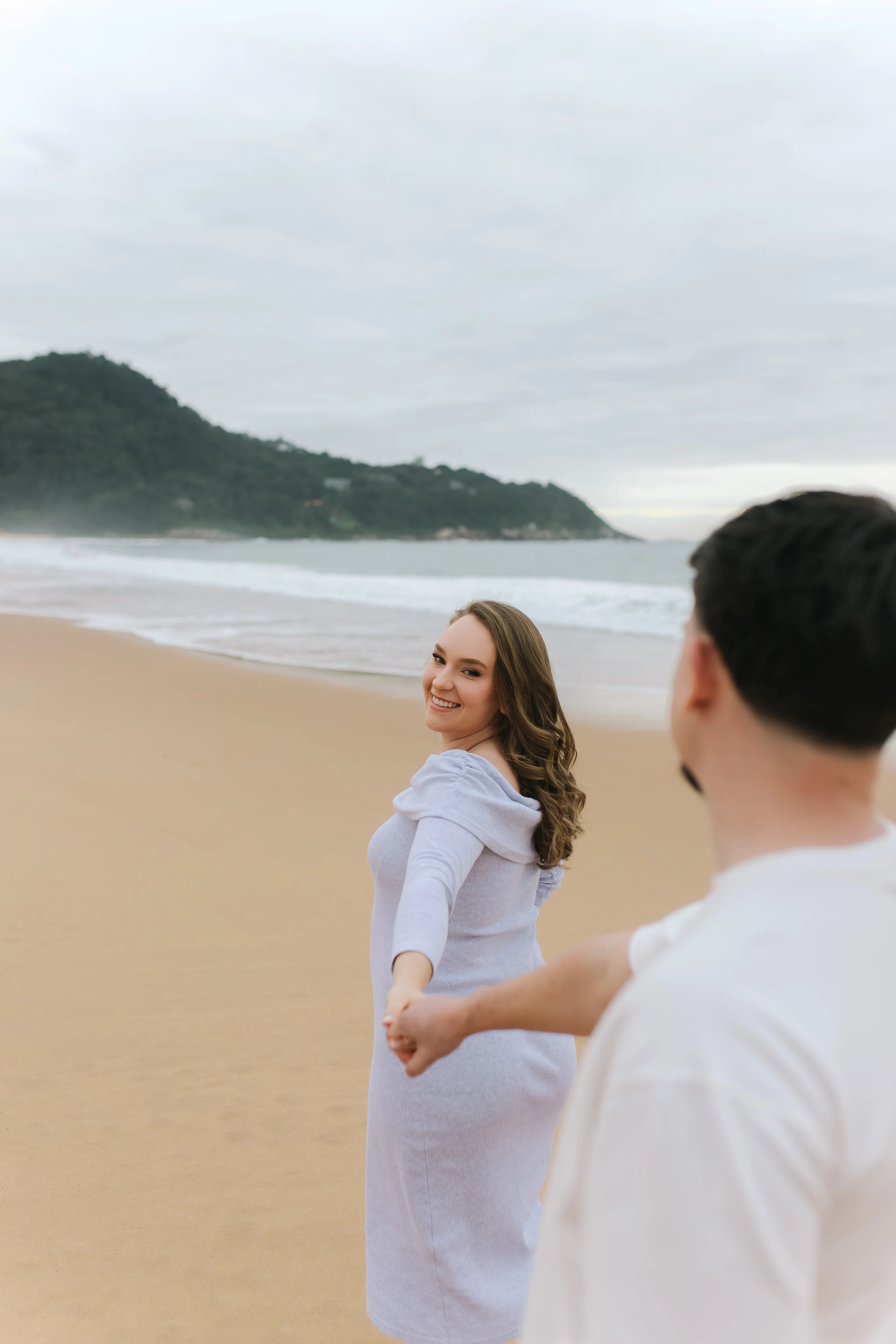 Gestante de mãos dadas com o marido na praia