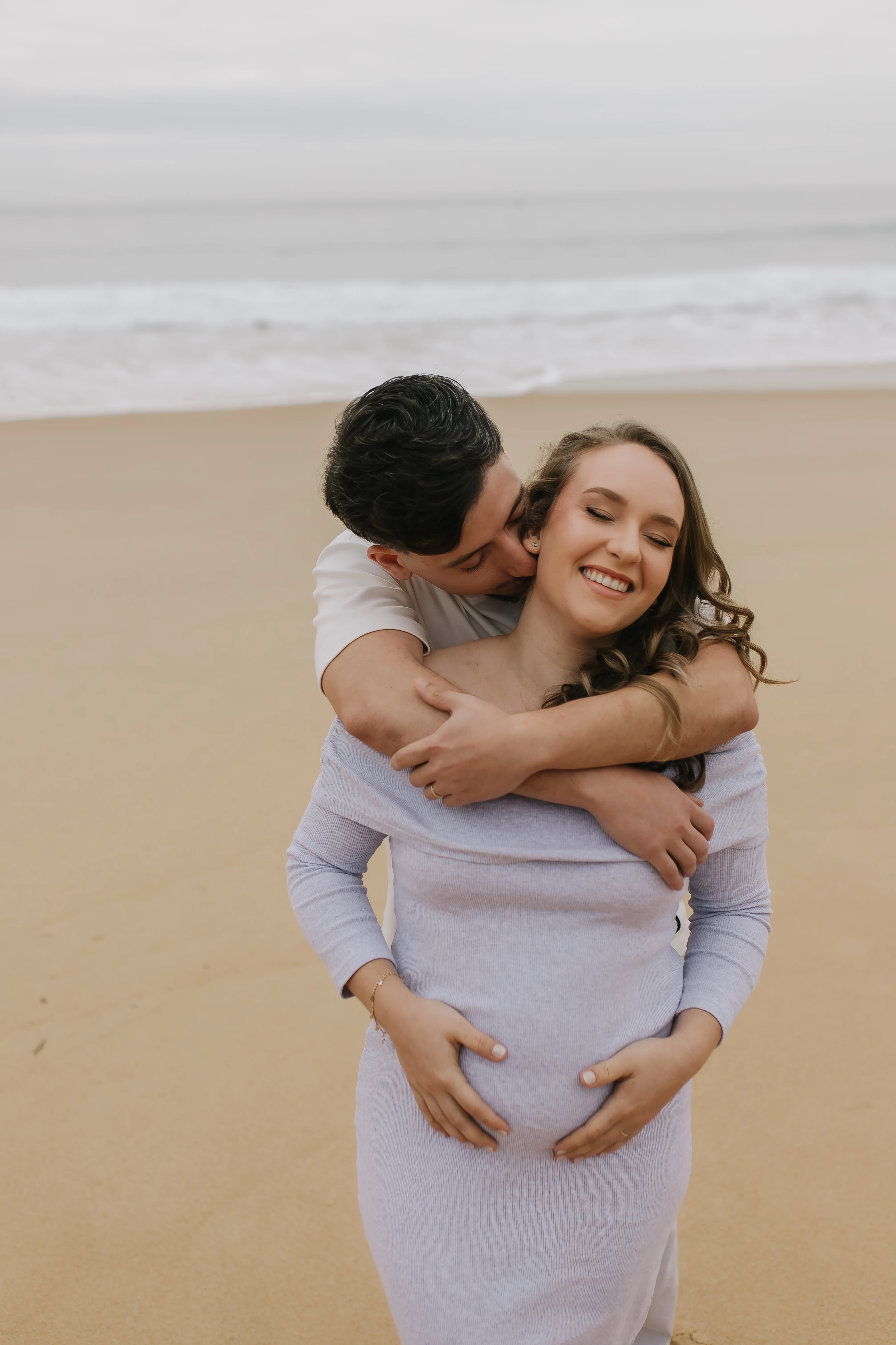 Pai abraça a gestante por trás, com as mãos na barriga