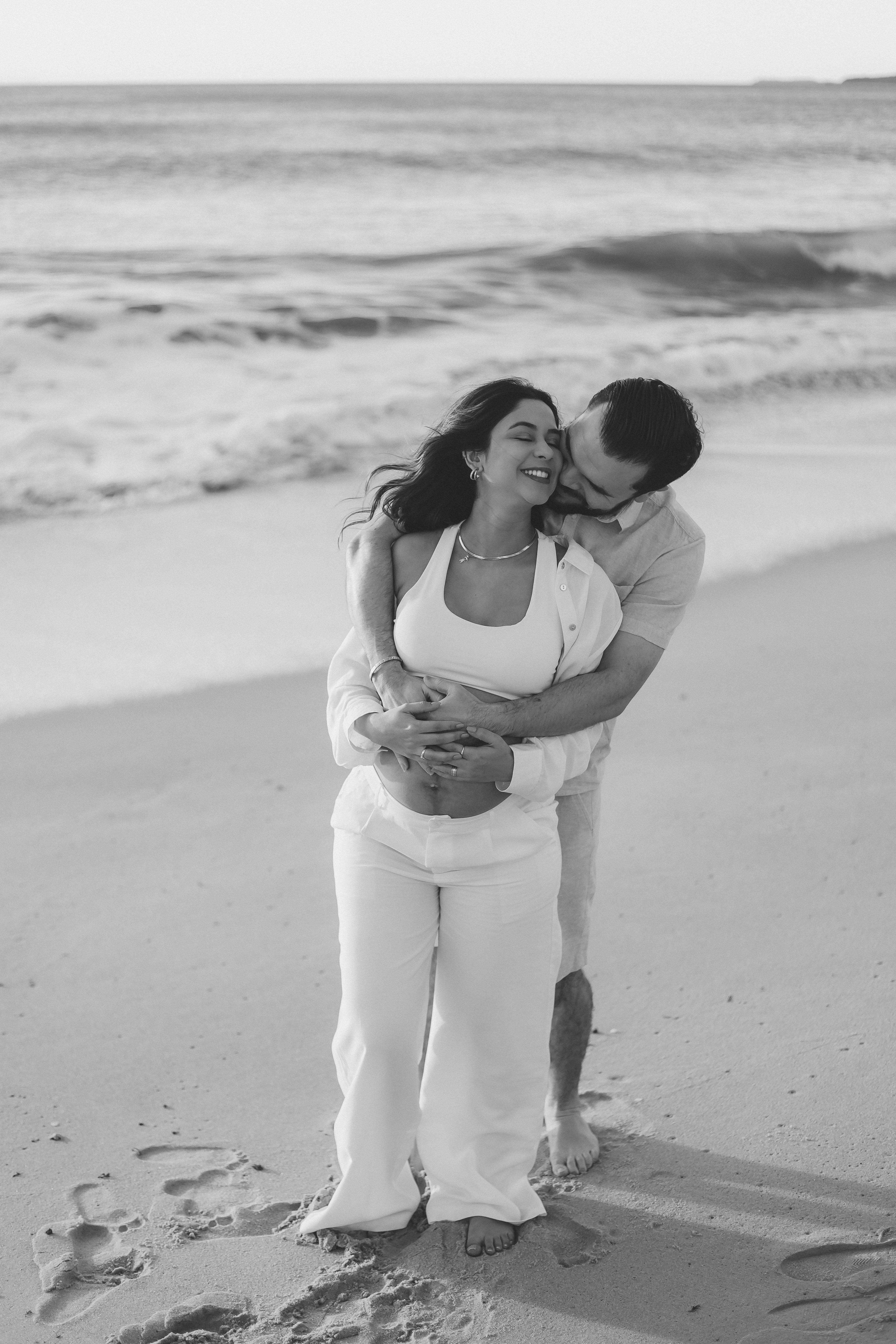 Casal gestante abraçado na praia em P&B